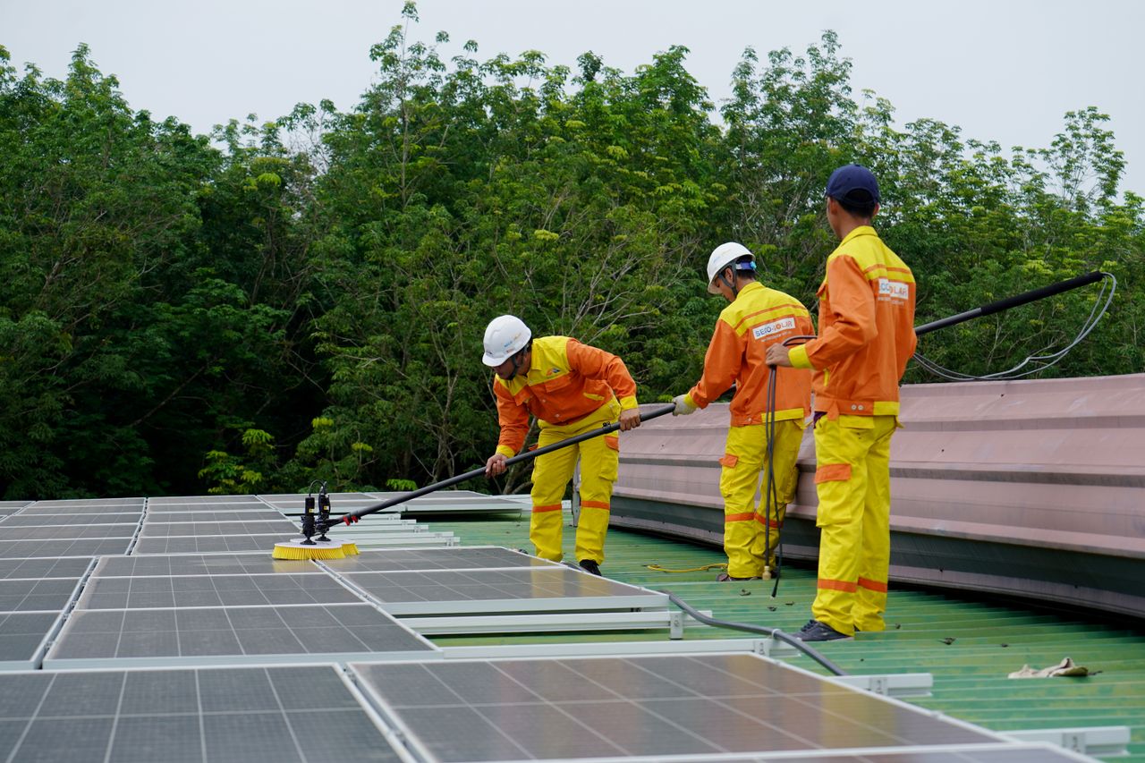 why-choose-us Three technicians in uniforms and hardhats clean rooftop solar panels in a renewable energy project.