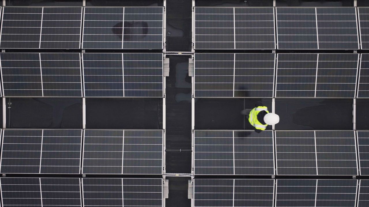 hero-img-02 Aerial view of a worker inspecting solar panels on a rooftop, promoting renewable energy.